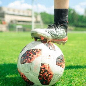 Close-up of a soccer ball with a player's foot on it, set on a vibrant green soccer field during a sunny day.